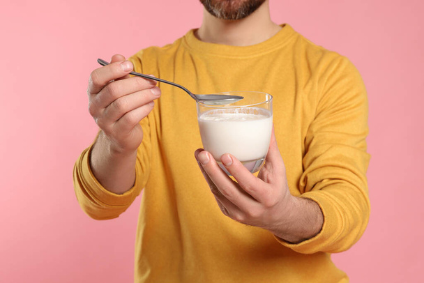 Man with delicious yogurt and spoon on pink background, closeup - Foto, Imagen