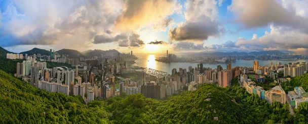Κορυφή εναέρια άποψη του ορίζοντα Χονγκ Κονγκ και cityscape με ηλιοβασίλεμα. Καταπληκτικό πανόραμα από ψηλά κτίρια και σύγχρονους πύργους και ουρανό που αντανακλά στο λιμάνι. Νήσος Χονγκ Κονγκ και χερσόνησος Kowloon. - Φωτογραφία, εικόνα