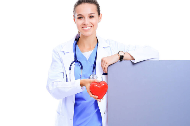 Positive female doctor standing with stethoscope and red heart symbol. - Fotografie, Obrázek