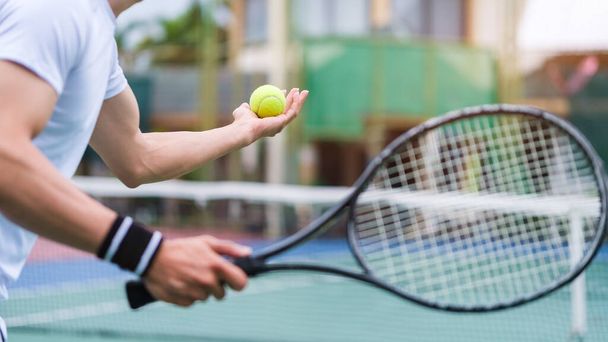 Tiro recortado de jugador de tenis masculino con raqueta y pelota preparándose para servir al comienzo del juego o partido. - Foto, Imagen
