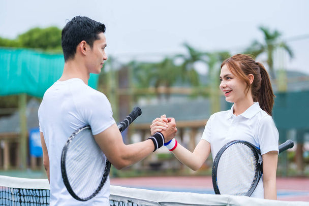 Tiro de dos jugadores de tenis felices estrechando la mano sobre la red después de un partido competitivo. - Foto, Imagen