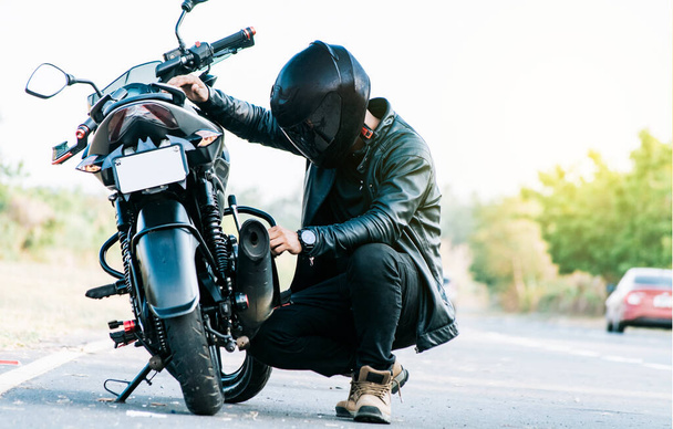 道路上のオートバイを固定するオートバイ主義者。バイカーは道路でバイクを修理男は道路で彼のオートバイをチェック - 写真・画像