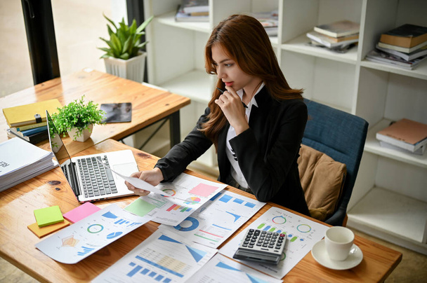 Een professionele en mooie Aziatische zakenvrouw of vrouwelijke financieel medewerker werkt aan een financieel rapport en analyseert financiële gegevens aan haar bureau in het kantoor. - Foto, afbeelding