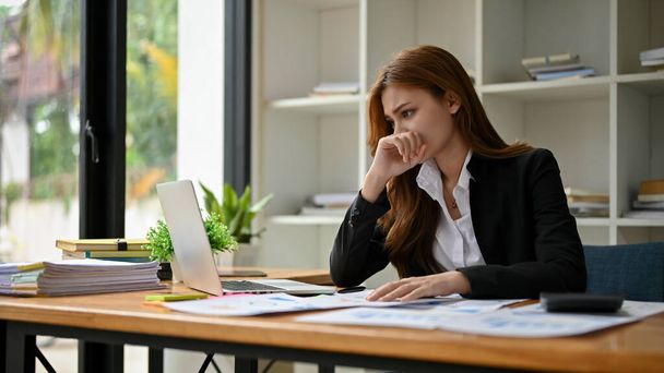 Une jeune femme d'affaires asiatique stressée et inquiète analysant les données financières de son ordinateur portable et travaillant sur des rapports financiers à son bureau. - Photo, image