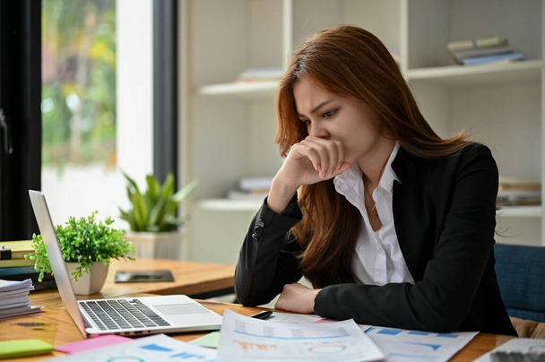 Een doordachte en gestreste Aziatische zakenvrouw richt zich op het werken business financiële gegevens rapporten aan haar bureau in het kantoor. - Foto, afbeelding