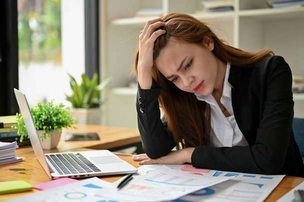 Een gestresste en gefrustreerde Aziatische zakenvrouw voelt zich ontevreden en bezorgd over haar financieel plan, lijdt aan hoofdpijn en wordt overwerkt. - Foto, afbeelding