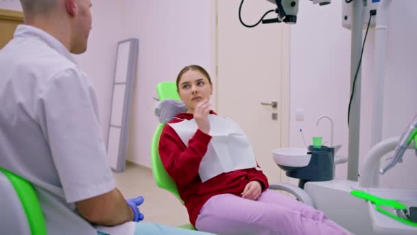 järkyttynyt naispotilas hammaslääkärin vastaanotolla valittaa hammassärystä ja karieksesta, joka pitelee poskiaan hammaslääkärin vastaanotolla - Materiaali, video