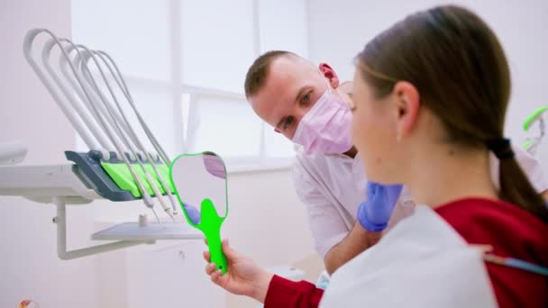 Femme heureuse regardant miroir jouissant de dents saines et propres beau sourire après le traitement clinique dentaire - Séquence, vidéo