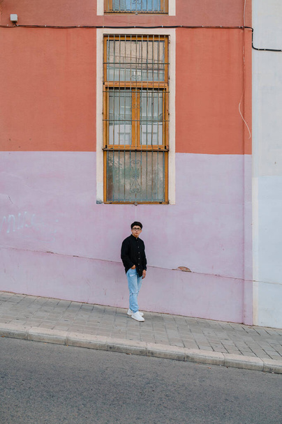 Junger Transgender mit Brille lehnt an einer Wand, während er draußen auf der Straße posiert. - Foto, Bild