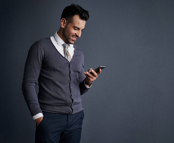 Communiceren met klanten via mobiele apps. Studio shot van een stijlvolle jonge zakenman met behulp van een mobiele telefoon tegen een grijze achtergrond - Foto, afbeelding