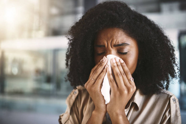 Que puis-je faire pour me débarrasser de cette grippe ? une jeune femme d'affaires se mouchant avec un mouchoir tout en travaillant dans un bureau moderne - Photo, image