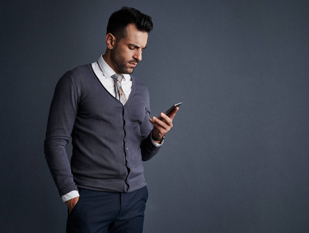 Produktivitätssteigerung durch Vernetzung. Studioaufnahme eines stylischen jungen Geschäftsmannes mit einem Mobiltelefon vor grauem Hintergrund - Foto, Bild