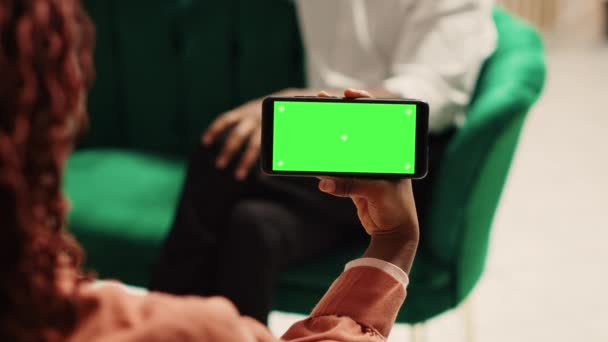 Afrikai amerikai nő kezében chroma kulcs zöld képernyő gúnyolódik okostelefon táj módban ül a hangulatos kanapén. A turisták várják az elegáns szálloda társalgóban, hogy ellenőrizze - Felvétel, videó