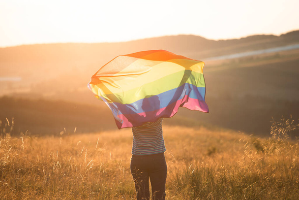 Woman holding a Gay Rainbow Flag in magic sunset. Happiness, freedom and love concept for same sex couples - Foto, afbeelding