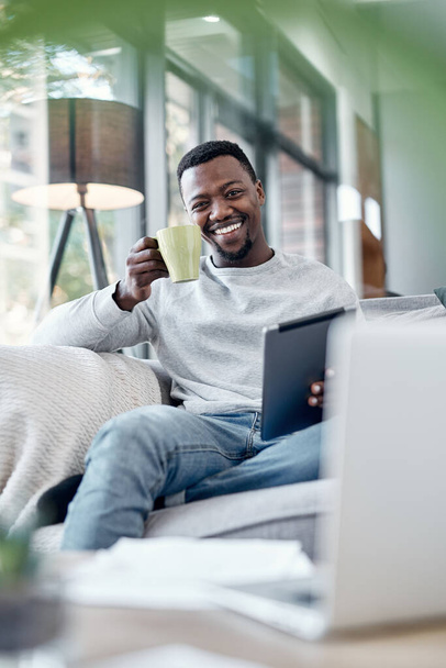 Portrait, coffee and tablet with a black man on a sofa, sitting in the living room of his home to relax. Smile, technology and internet with a happy person relaxing in a house to browse social media. - Photo, image