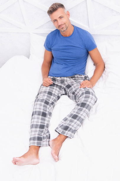 Happy man resting in bed. Man in sleepwear relaxing on white bedclothes. Man having rest in morning. Man enjoying rest in bed. Morning rest. - Zdjęcie, obraz
