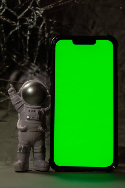 Plastic toy figure astronaut with mobile phone chroma key green screen for your advertisement Copy space. Concept of out of earth travel, private spaceman commercial flights. Space missions and - Фото, изображение