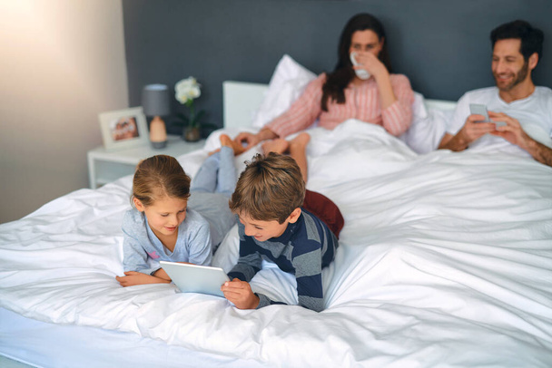 Theyre feeling too comfy to leave the bed. an adorable little girl and boy using a tablet together while their parents are chilling in bed at home - Foto, afbeelding