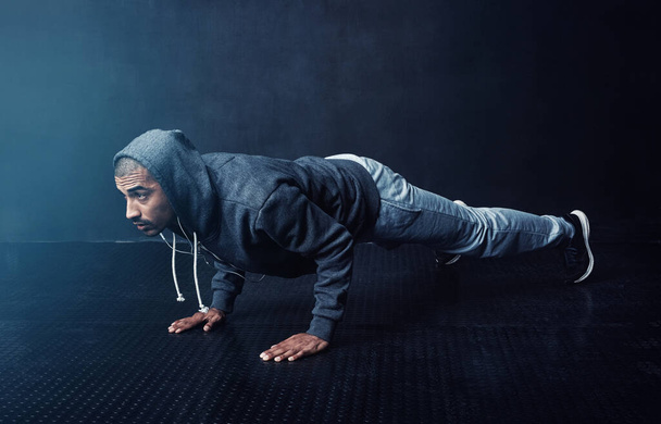 Elke reputatie wordt sterker. Studio shot van een jonge man doen pushups tegen een donkere achtergrond - Foto, afbeelding