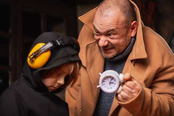 A man shakes an alarm clock in front of a young tired boy. The process of misperception concept. - Фото, зображення