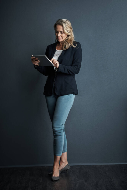 Manejando sus planes para el éxito. Captura de estudio de una mujer de negocios madura usando una tableta digital sobre un fondo gris - Foto, Imagen