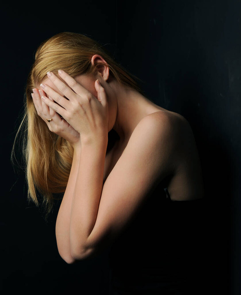 close-up portret van mooie jonge blonde model met blond haar, gebaar arm poses, geïsoleerd tegen een donker zwart studio achtergrond. - Foto, afbeelding