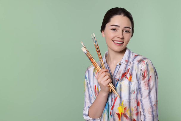 Woman with paintbrushes on pale green background, space for text. Young artist - Foto, immagini