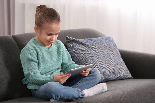 Klein meisje met tablet op de bank thuis. Internetverslaving - Foto, afbeelding