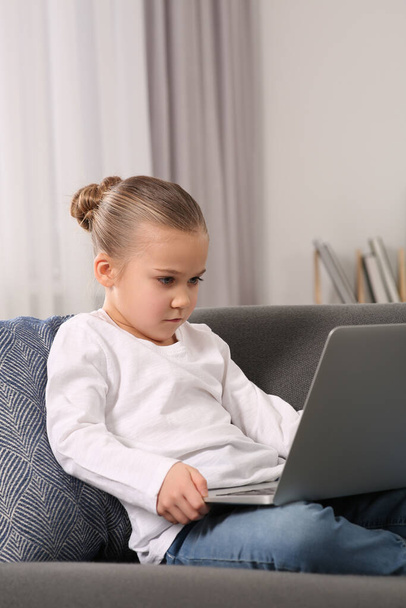 Little girl using laptop on sofa at home. Internet addiction - Foto, Imagem