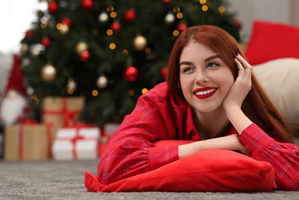 Beautiful young woman lying on floor near Christmas tree at home, space for text - Фото, зображення