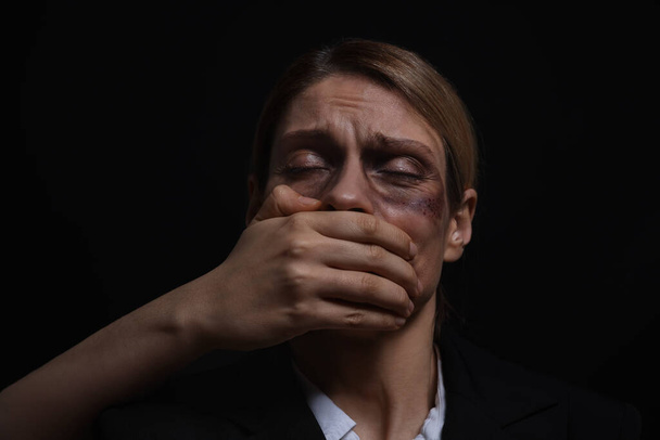 Porywacz zakrywający usta kobiety wziętej jako zakładniczka na ciemnym tle - Zdjęcie, obraz