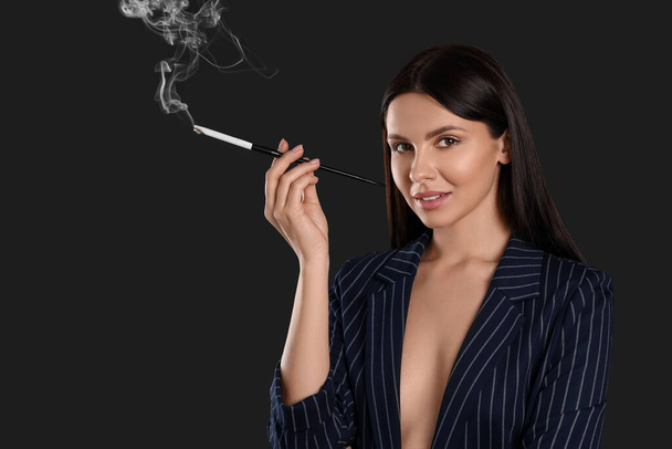 Woman using long cigarette holder for smoking on black background - Foto, afbeelding