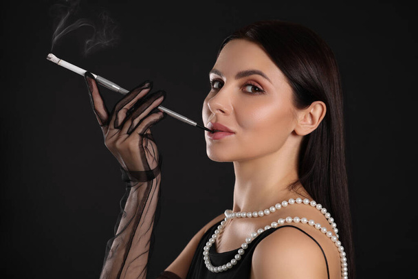 Woman using long cigarette holder for smoking on black background - Photo, Image
