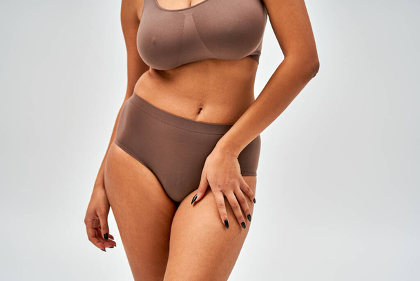 Cropped view of african american woman in modern brown panties and bra touching hip and standing isolated on grey, self-acceptance and body positive concept  - Zdjęcie, obraz