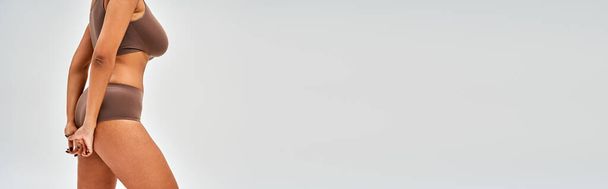 Vista cortada de mulher americana africana sedutora em lingerie marrom moderno de pé isolado em cinza, auto-aceitação e conceito de corpo positivo, banner com espaço de cópia - Foto, Imagem