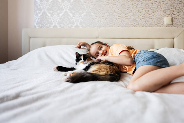 Cute little girl playing with her cat on the bed at home - Zdjęcie, obraz