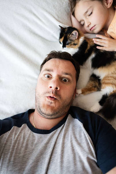 Vista superior de padre e hija durmiendo juntos en la cama en casa con el gato y divertirse. - Foto, imagen