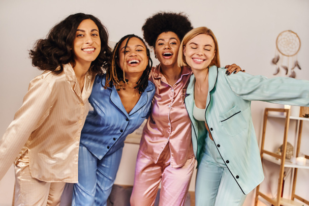 Smiling multiethnic girlfriends in colorful pajama looking at camera, hugging each other and having fun during slumber party at home, bonding time in comfortable sleepwear - Фото, зображення