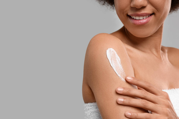 Young woman applying body cream onto arm on grey background, closeup. Space for text - Φωτογραφία, εικόνα