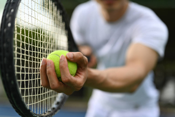 Κοντινό πλάνο του ανδρικού παίκτη του τένις χέρι κρατώντας μπάλα του τένις και ρακέτα, ξεκινώντας που ή εξυπηρετούν μπάλα κατά τη διάρκεια του αγώνα. - Φωτογραφία, εικόνα