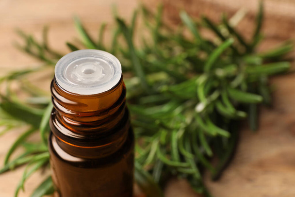 Bottle with essential oil and fresh rosemary against blurred background, closeup. Space for text - Fotó, kép