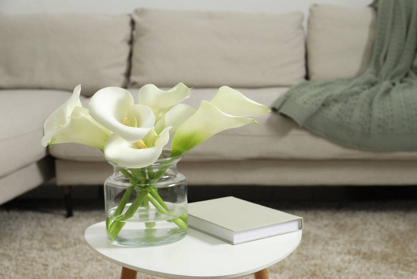 Beautiful calla lily flowers in glass vase and book on white table indoors - Photo, Image