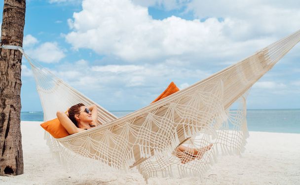 Young woman relaxing in wicker hammock on the sandy beach on Mauritius coast and enjoying wide ocean view waves. Exotic countries vacation and mental health concept image. - Фото, зображення