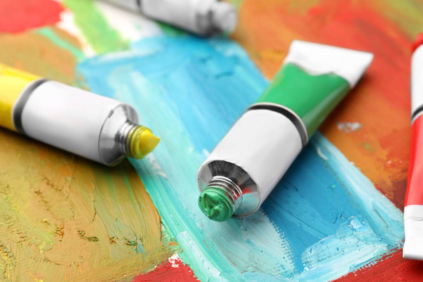 Tubes of colorful oil paints on canvas with abstract painting, closeup - Fotoğraf, Görsel