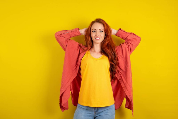 Sarı stüdyo arka planında duran kızıl saçlı tatmin olmuş kadın kafa rahatlatıcı bir şekilde el ele tutuşuyor. - Fotoğraf, Görsel