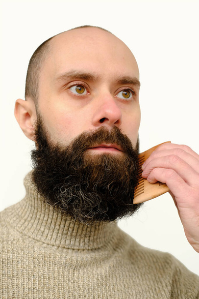 close-up of male face, young bearded and mustachioed man, guy with 25 - 30 years combs his thick beard, concept of mustache and beard stubble care products, hairline hygiene on lower part of face - Photo, Image