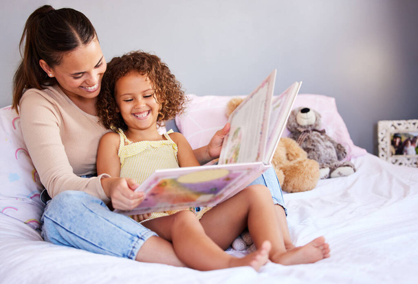 Smile, book and mother with daughter in bedroom for storytelling, fantasy or creative. Education, learning and love with woman reading to young girl in family home for fairytale, literature and relax. - 写真・画像