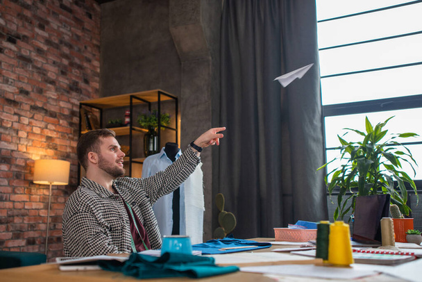 A man throws a paper airplane up high at the ceiling and then gets back to work as he is bopping his head to the music while measuring out fabric. Portrait - Foto, imagen