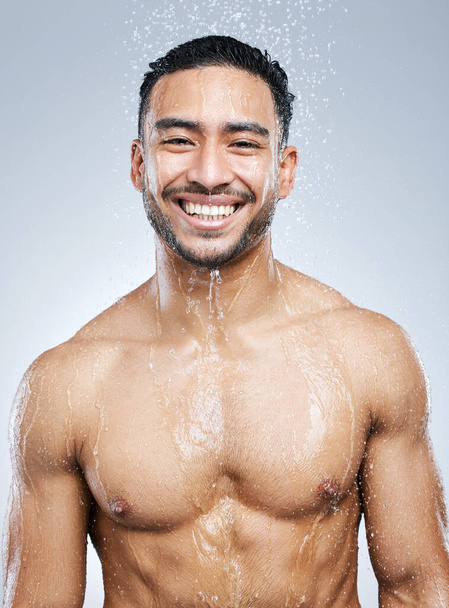 Portrait of man in shower with smile, cleaning and hygiene for healthy body and studio backdrop. Water, skin and hair care, happy male model washing with skincare on background with bathroom spa - Zdjęcie, obraz