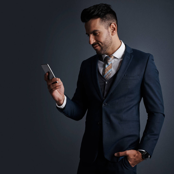 Створення операцій мобільного бізнесу. Студійний знімок стильного молодого бізнесмена, який використовує мобільний телефон на сірому фоні
 - Фото, зображення